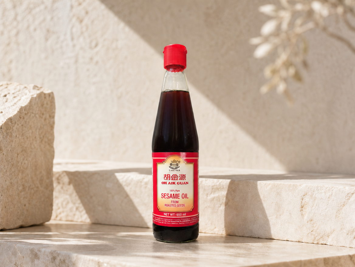 Oh Aik Guan sesame oil bottle in warm sunlight — the same silhouette and red cap the brand ships, shown clear of surface haze.